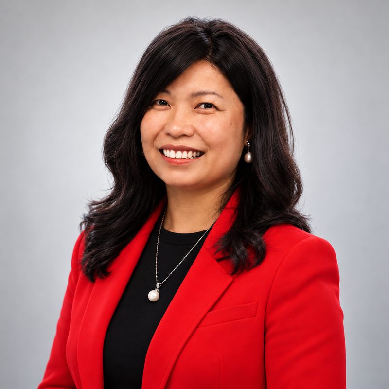 Terri Abellera, smiling, in a red blazer and pearl necklace